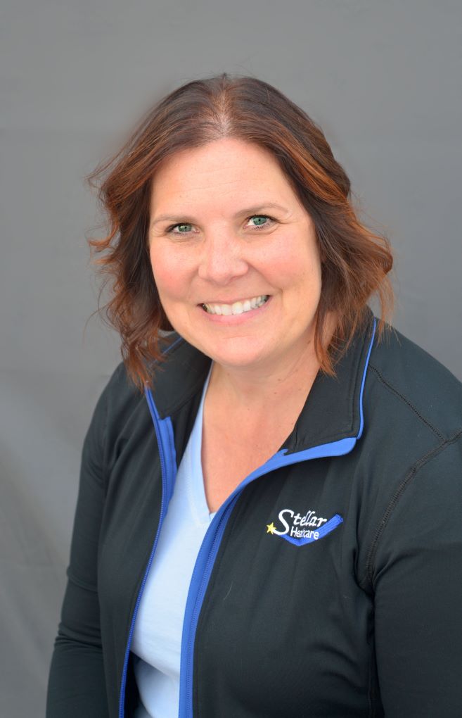 Melissa Erdmann sitting with a Stellar Healthcare black jacket with logo, smiling.