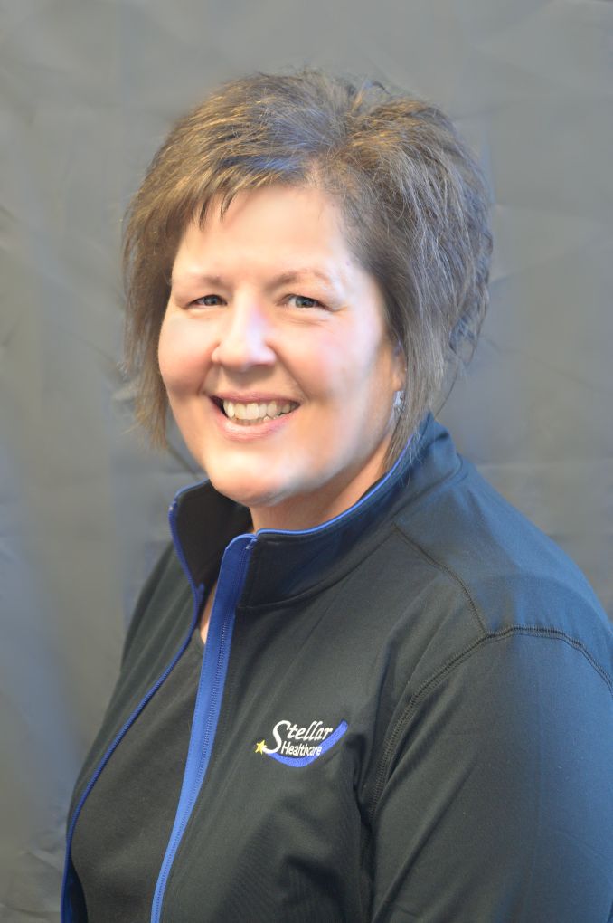 Melissa Erdmann sitting with her Stellar Healthcare black jacket with logo, smiling.