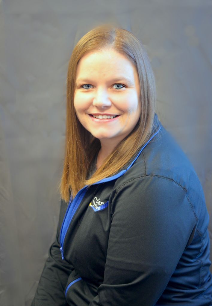 Melissa Erdmann sitting with her Stellar Healthcare black jacket with logo, smiling.