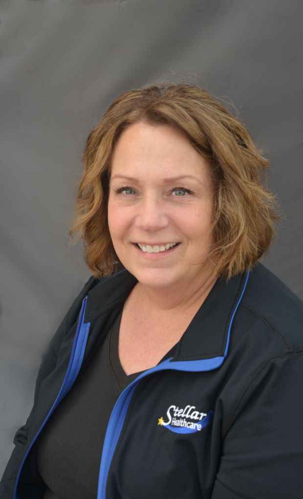 Melissa Erdmann sitting with her Stellar Healthcare black jacket with logo, smiling.