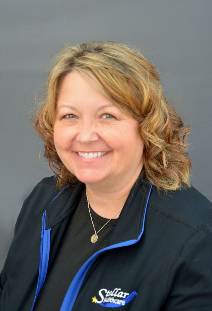 Melissa Erdmann sitting with her Stellar Healthcare black jacket with logo, smiling.